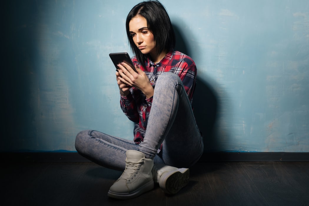 A photo of a young girl sitting in the dark gazing at her phone.