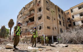 Israeli security forces gather outside a building that was hit by an Iranian missile in Israel's central city of Holon on June 19, 2025. A hospital in southern Israel and two towns near Tel Aviv were struck after a barrage of Iranian missiles early on June 19, with rescuers reporting at least 47 people injured in the latest attacks. (Photo by Jack GUEZ / AFP)