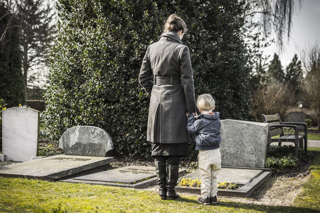 26592865 - A photo of a woman and child looking at gravestone on graveyard