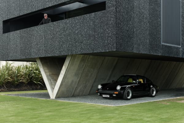 An image of a house installed on concrete V-shaped stilts, with a small car parked underneath, in Piha.