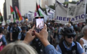 A person films people holding Palestinian flags during a protest to demand reproductive justice, defend the rights of trans and queer people and demand a ceasefire in Gaza on the eve of the Democratic National Convention (DNC) at the United Center in Chicago, Illinois, on August 18, 2024. (Photo by MATTHEW HATCHER / AFP)