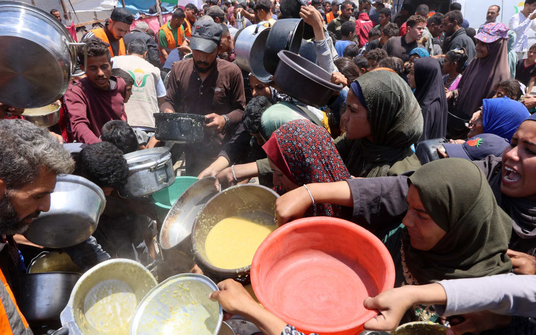 Palestinians reach out for food being distributed at a displacement camp near Gaza City's port on 22 May, 2025.