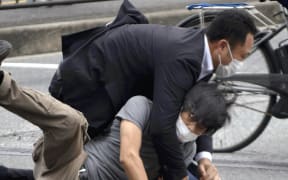 A man suspected of shooting Japanese Prime Minister Shinzo Abe at Yamato Saidaiji Station in Nara Prefecture on July 8, 2022 is wrestled to the ground.  67-year-old Abe has reportedly been shot in the chest during a stumping tour in Nara in the morning on July 8.