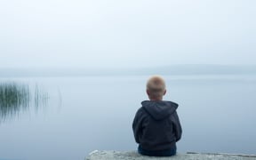 47556115 - sad child sitting alone by lake in a foggy day, back view