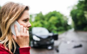A woman on a mobile phone at the scene of a car accident.