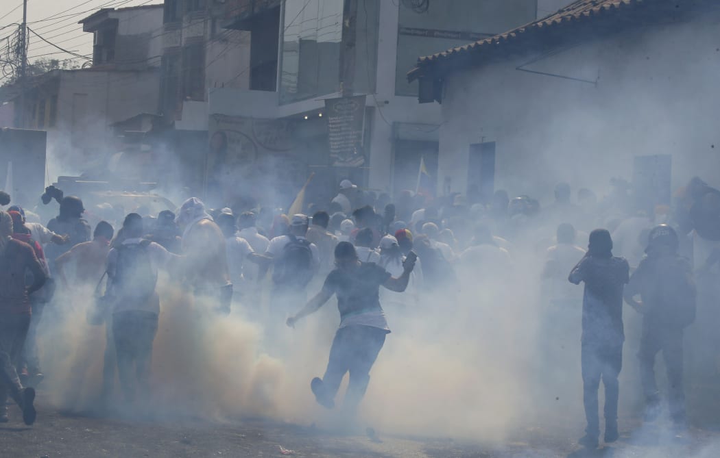 Demonstrators are engulfed by a cloud of tear gas fired by Bolivarian National Guard officers during clashes in Urena, Venezuela, near the border with Colombia, Saturday, Feb. 23, 2019.