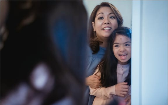 Image of mother and daughter looking at themselves in the mirror.