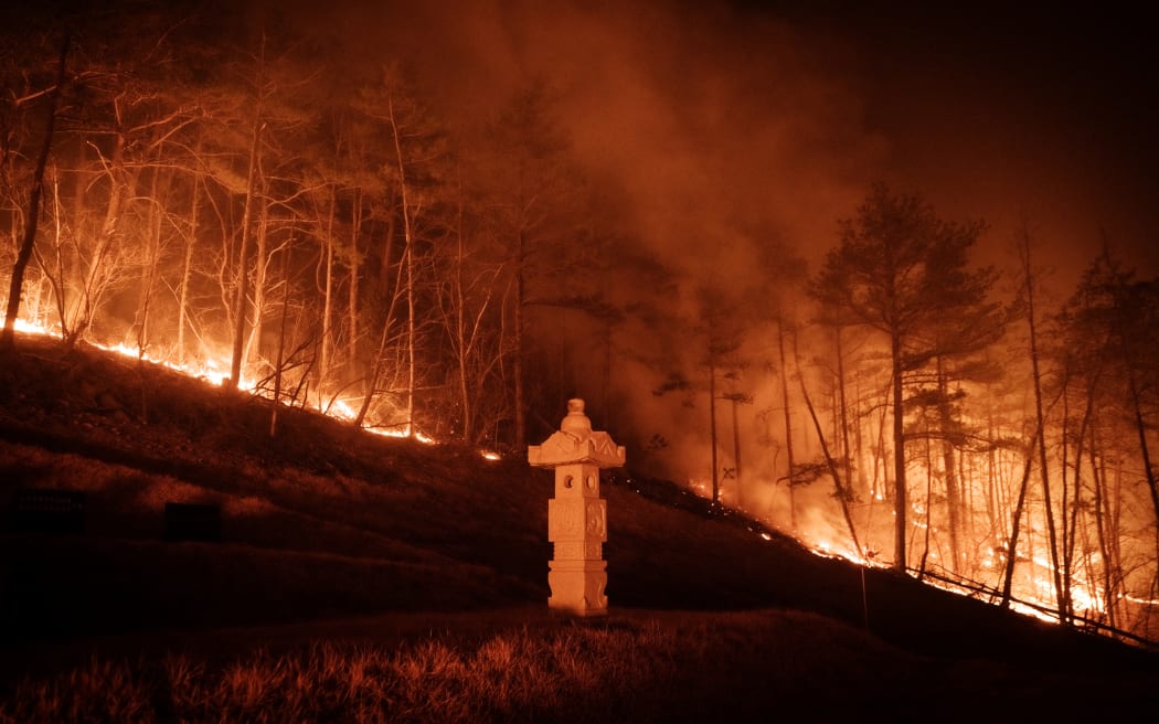 A wildfire is seen next to a stone lantern of family tomb in Andong on March 26, 2025. At least 18 people have been killed in one of South Korea's worst wildfire outbreaks, with multiple blazes burning and causing "unprecedented damage", the acting president said. (Photo by YASUYOSHI CHIBA / AFP)
