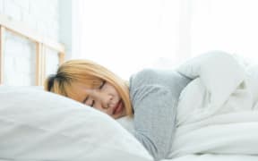 An Asian woman in bed with her eyes closed