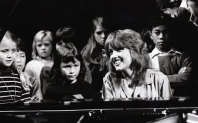 Sharon O'Neill (1978) plays piano surrounded by children.