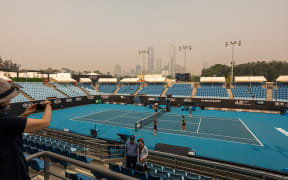 Tourists pose for a photo in the stands of one of the outside courts at Melbourne Park as the horizon is covered with thick smoke haze in Melbourne on January 15, 2020, ahead of the Australian Open tennis tournament.