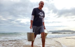 James collects seawater by hand from Cable Bay in Northland