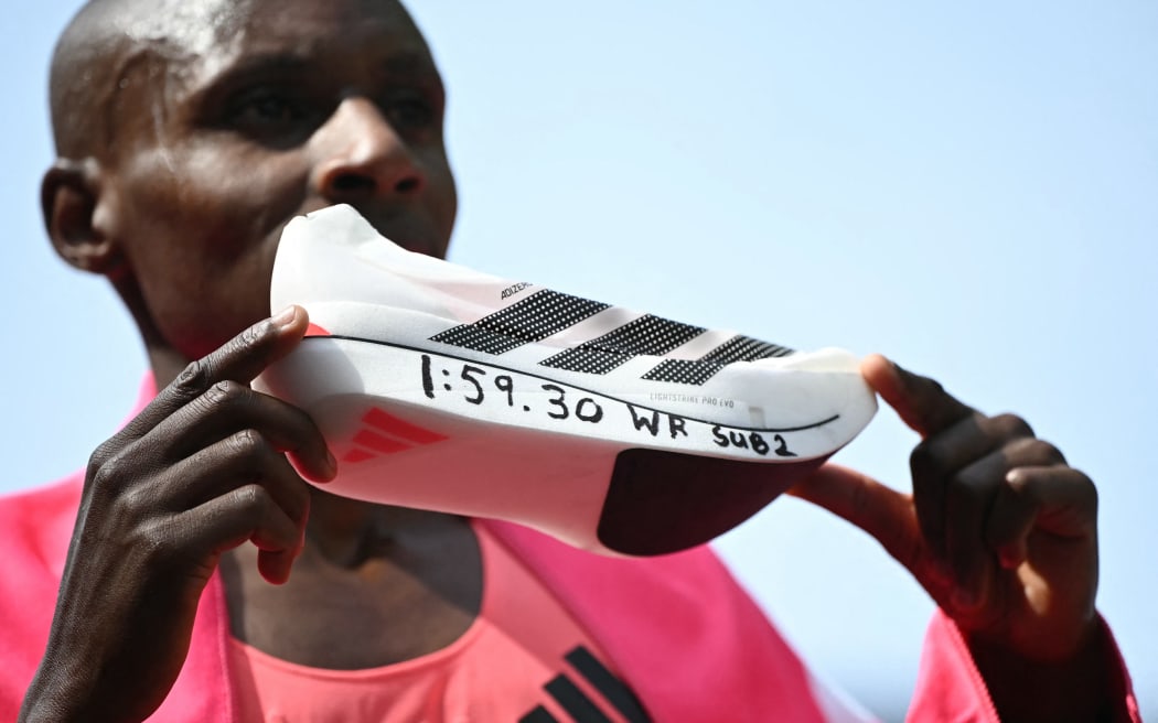 Kenya's Sabastian Sawe poses with his new world record time written on his running shoe at the finish of the 2026 London Marathon.