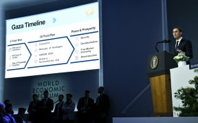 US businessman Jared Kushner speaks as a "Gaza Timeline" is displayed on a giant screen at the "Board of Peace" meeting during the World Economic Forum (WEF) annual meeting in Davos on January 22, 2026. US President Donald Trump will show off his new "Board of Peace" at Davos on January 22, 2026 burnishing his claim to be a peacemaker a day after backing off his own threats against Greenland. Originally meant to oversee the rebuilding of Gaza after the war between Hamas and Israel, the board's charter does not limit its role to the Strip, and has sparked concerns that Trump wants it to rival the United Nations.
