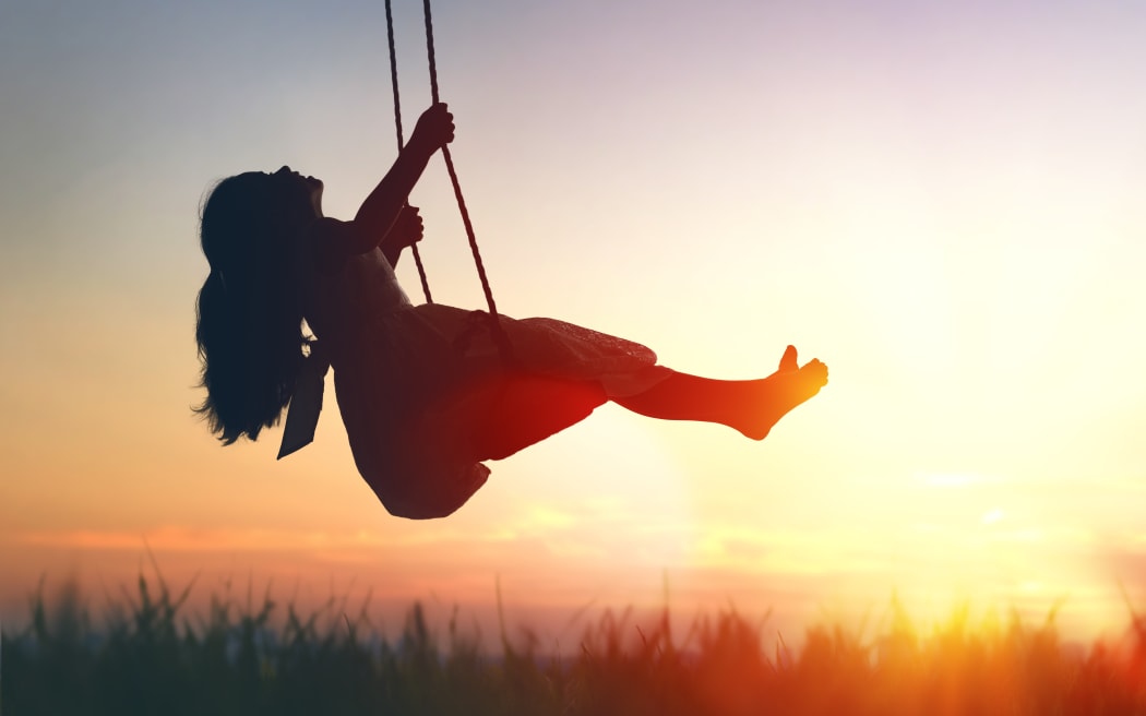 Happy laughing child girl on swing in sunset summer.