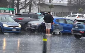 Young man helping elderly shoppers in the rain in Rotorua