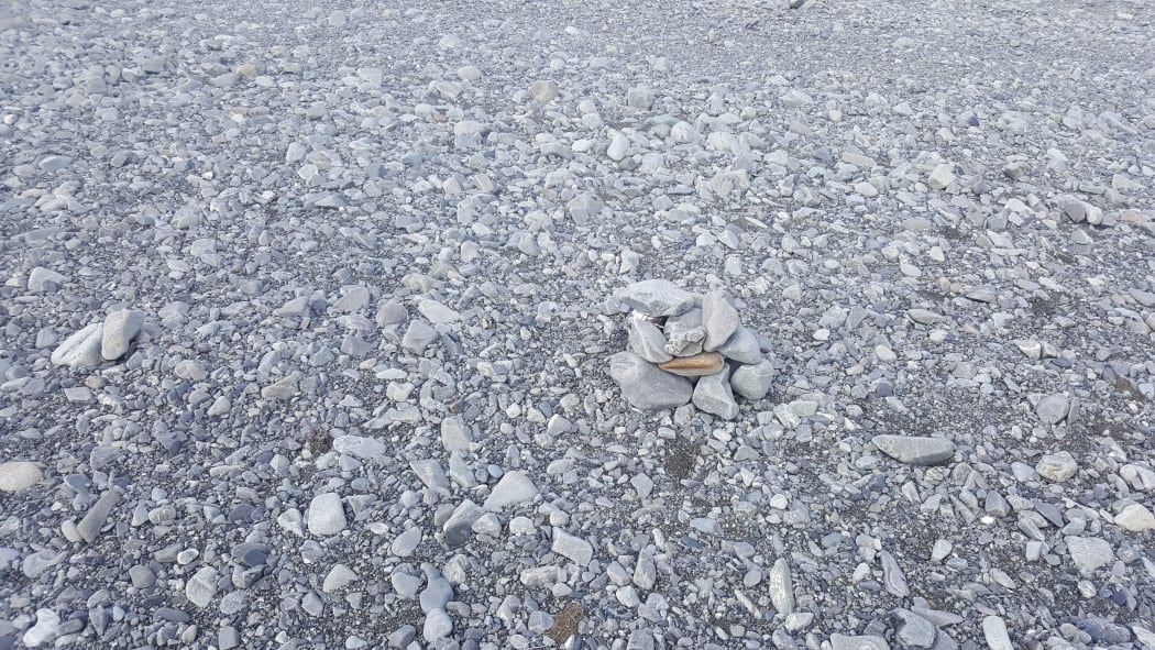 An almost invisible wrybill sitting amongst grey rocks on a river bed.