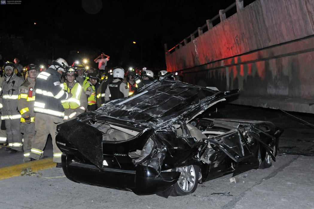 Rescue workers stand before a destroyed car crushed by a bridge which collapsed in the 7.8 magnitude quake.