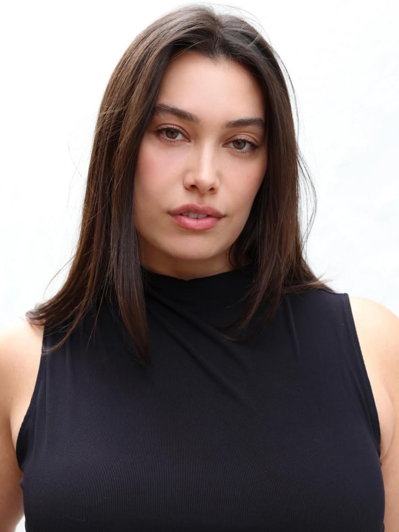 Isabella Moore - a Pasifika woman with long brown hair - wears a sleeveless black top and looks seductively at the camera.