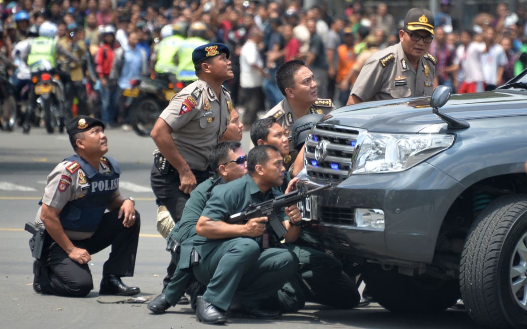 Police take up position behind a vehicle as they pursue suspects after a series of blasts hit the Indonesia capital Jakarta.