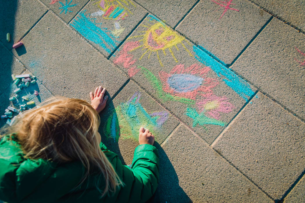 Child drawing outside on footpath with chalk.