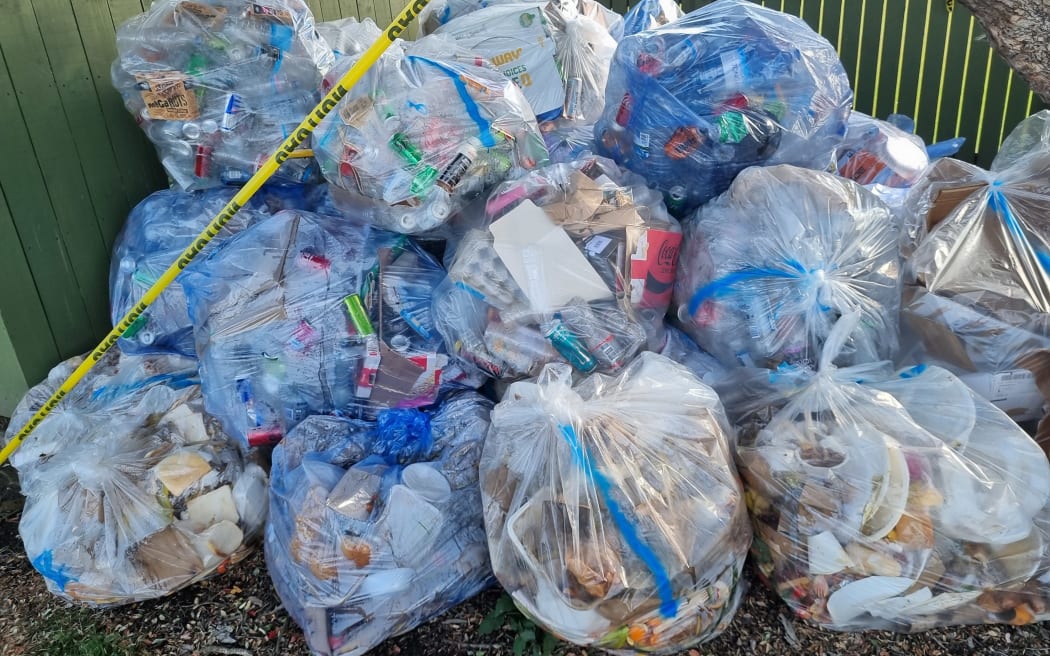 A bunch of clear rubbish sacks stacked on top of each other with a row of yellow caution tape across them.