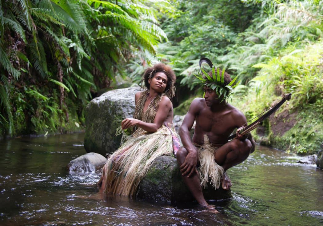 A man and a woman in tradional Ni-Vanuatu clothing sit on a rock in a river