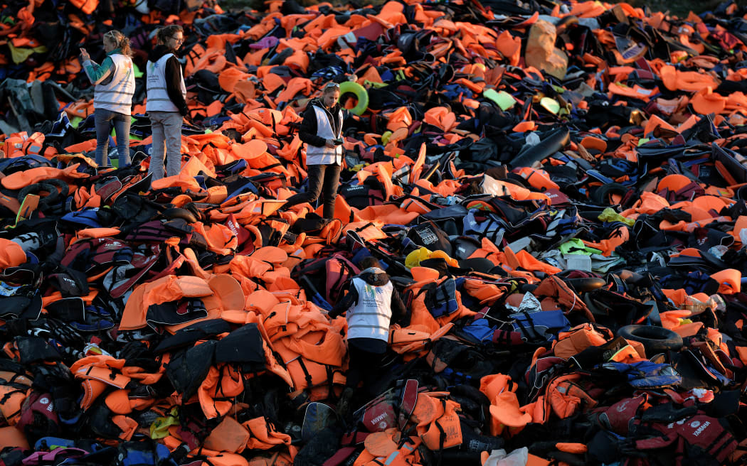 Volunteers stand on a pile of lifejackets left behind by refugees and migrants who arrived to the Greek island of Lesbos after crossing the Aegean sea.