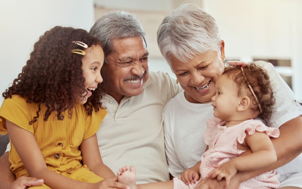 Mixed race grandparents enjoying weekend with granddaughters in home living room. Adorable smiling hispanic girls bonding with grandmother and grandfather. Happy seniors and children sitting together.