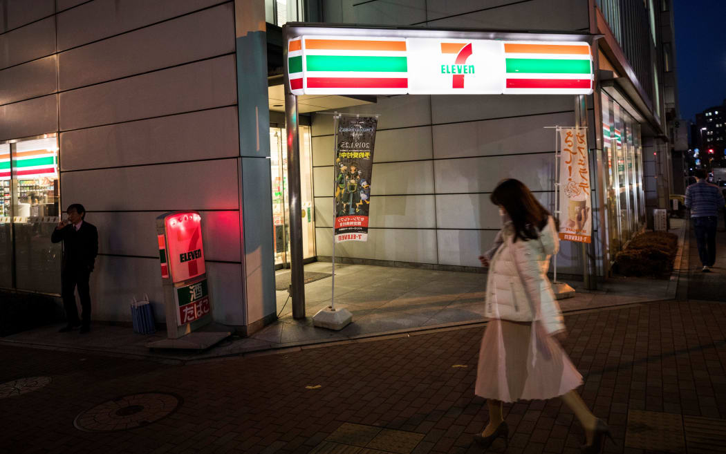 A woman walks past a 7-Eleven convenience store in Tokyo on January 22, 2019. - Japan's omnipresent convenience stores are preparing to stop selling pornographic magazines before waves of tourists visit the nation for the Olympic Games and the Rugby World Cup.