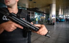 A Turkish anti-riot police officer (L) stands guard as people walk past near the explosion site at Ataturk airport International arrival terminal in Istanbul.