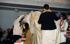 A mat is draped over Prime Minister Jacinda Ardern as part of the Samoan Ifoga ceremonial apology.