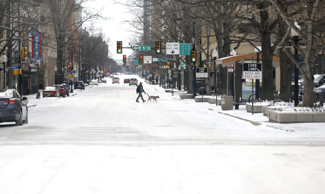 A man walks his dog in central Fort Worth, Texas, 16 February 2021, after a snow storm on brought historic cold weather and power outages.