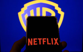 The Netflix logo appears on a mobile phone with the Warner Bros. icon visible in the background, in this photo illustration in Copenhagen, Denmark, on December 11, 2025. (Photo Illustration by Kristian Tuxen Ladegaard Berg/NurPhoto) (Photo by Kristian Tuxen Ladegaard Berg / NurPhoto via AFP)