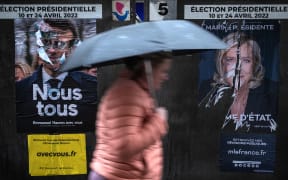 A pedestrian walks past campaign poster of French President Emmanuel Macron and presidential candidate Marine Le Pen of the far-right Rassemblement National party.