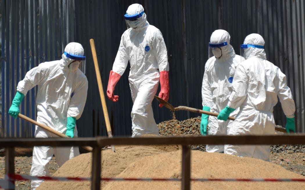 Health workers from the Liberian Red Cross shovel sand to absorb fluids from the bodies of Ebola victims in Monrovia.