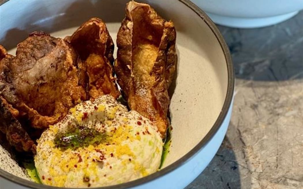 A bowl of tarama dip garnished with fried Jerusalem artichoke skins.