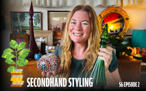 A smiling woman with long, wavy blonde hair stands in a cozy, vintage-styled room, holding a green glass bottle in one hand and a colourful mosaic bowl in the other. Behind her is a wooden sideboard decorated with framed art, retro ornaments, tall decorative bottles, plants, and a sunset-themed lamp. Text on the image reads: “SECONDHAND STYLING – S6 EPISODE 2.”