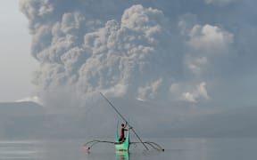 A youth living at the foot of Taal volcano rides an outrigger canoe while the volcano spews ash as seen from Tanauan town in Batangas province, south of Manila, on January 13, 2020.
