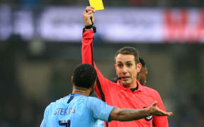 English football referee David Coote shows a yellow card.