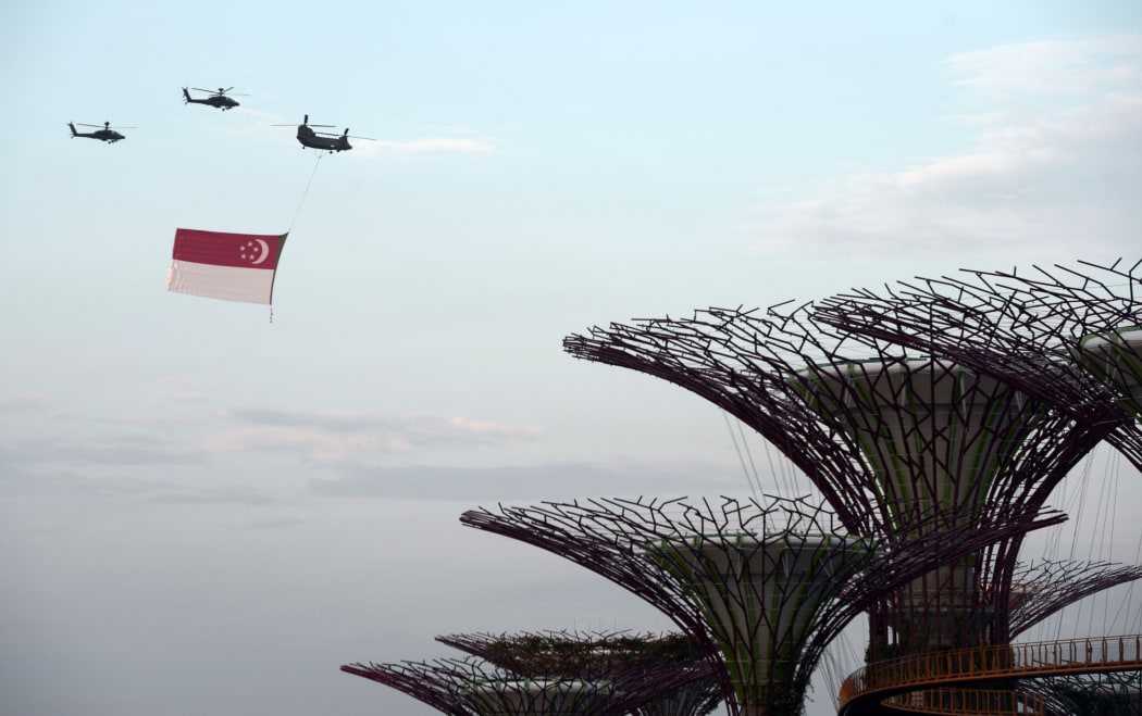 A Chinook helicopter (top R) from the Republic of Singapore Air Force flies a giant national flag over the Garden by the Bay dome