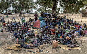 Families gather under the shade of a tree at an informal site where displaced people have assembled without assistance or shelter at Yolakot informal camp near Mingkaman, on February 14, 2026. South Sudan gained independence in 2011 but quickly descended into civil war between rival generals, Salva Kiir and Riek Machar. A power-sharing deal in 2018 brought relative peace, with Kiir as president and Machar his deputy. But the deal was never fully implemented, their forces never unified, and elections never held. Over the past year, Machar has been jailed and violence has erupted between their forces in several areas. The worst has been in Jonglei state, where some 280,000 people have been displaced since December, according to the United Nations. (Photo by Luis TATO / AFP)