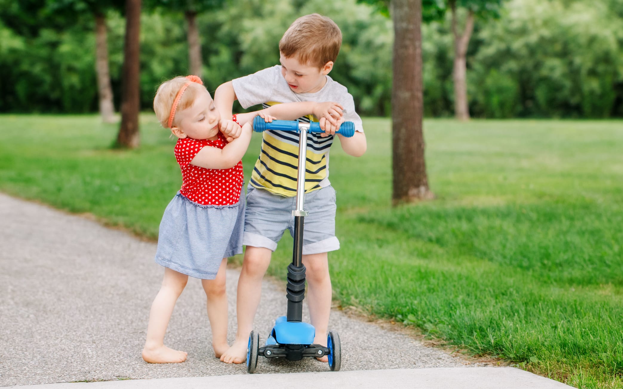 A photo of two little Caucasian preschool children fighting hitting each other. Boy and girl can not share one scooter. Older sibling brother not giving his toy to younger sister. Communication problems.