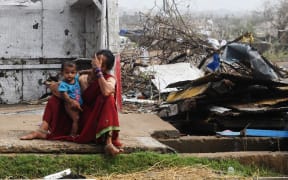 An Indian woman sits with her child next to storm-damaged buildings in Puri in the eastern Indian state of Odisha,
