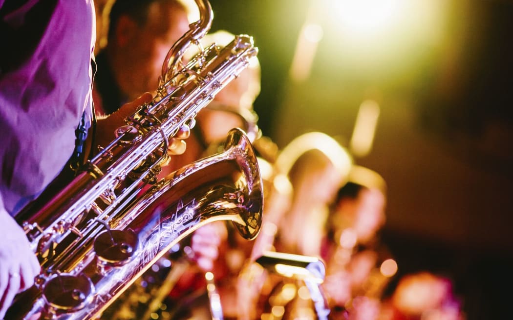 A close-up of a saxophone held by one of the band members during a jazz concert. Original public domain image from Wikimedia Commons