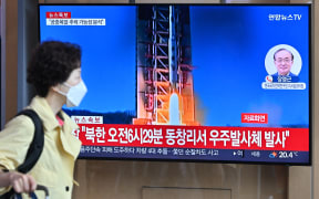 A woman walks past a television screen showing a news broadcast with file footage of North Korea's rocket launch, at the Seoul Railway Station in Seoul on May 31, 2023. North Korea launched its purported spy satellite on May 31, the South's military said, prompting confusion in Seoul as the city briefly issued an evacuation warning in error. (Photo by Jung Yeon-je / AFP)