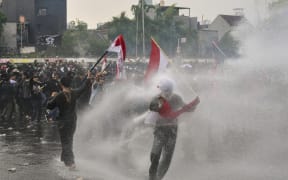 Students throw objects at the police while being sprayed with a water cannon during a protest outside the parliament building against lawmakers’ demands for higher allowances in Jakarta on August 28, 2025. (Photo by BAY ISMOYO / AFP)