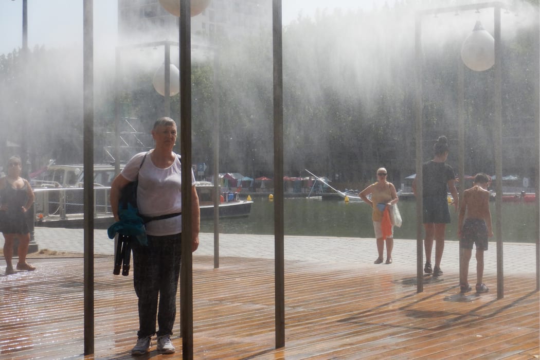 People stand under water atomisers at the Bassin de la Villette in Paris to cool off in a heatwave.