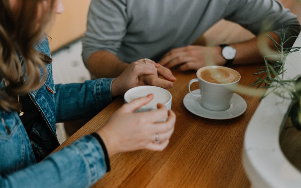 Image of two people having coffee together, their hands and the coffee are visible.