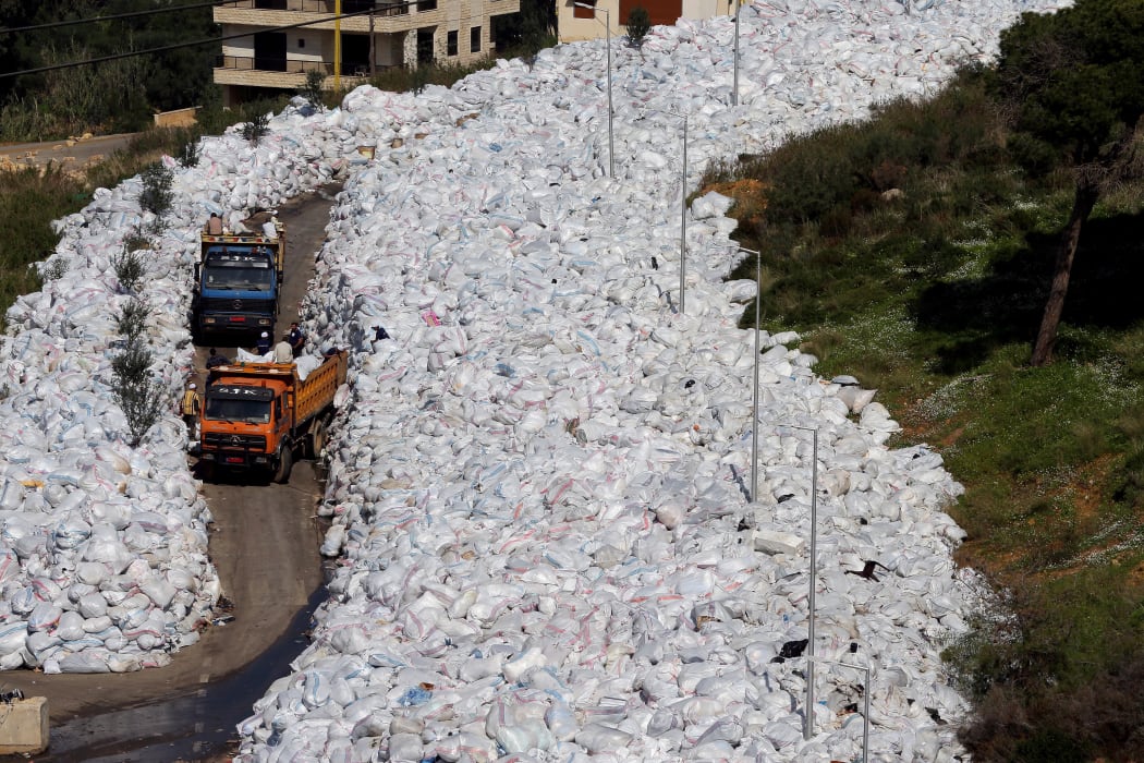 Rubbish trucks drive between a built up pile of waste on a street in Beirut's northern suburb of Jdeideh on February 25, 2016